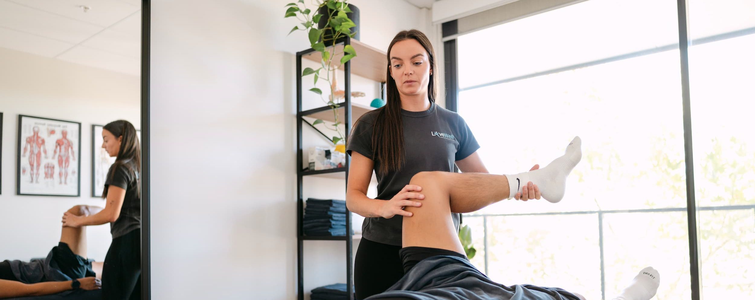 Live Well practitioner performing hip flexor and leg mobility assessment on patient in clinic