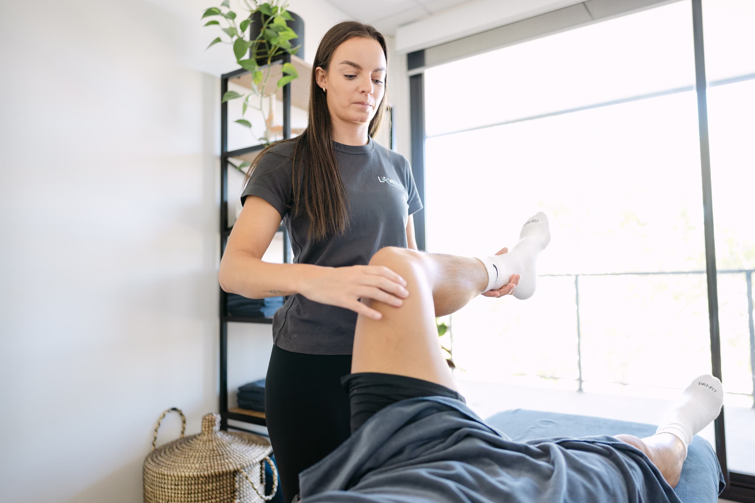 Live Well practitioner assessing patient's knee joint mobility and function on treatment table