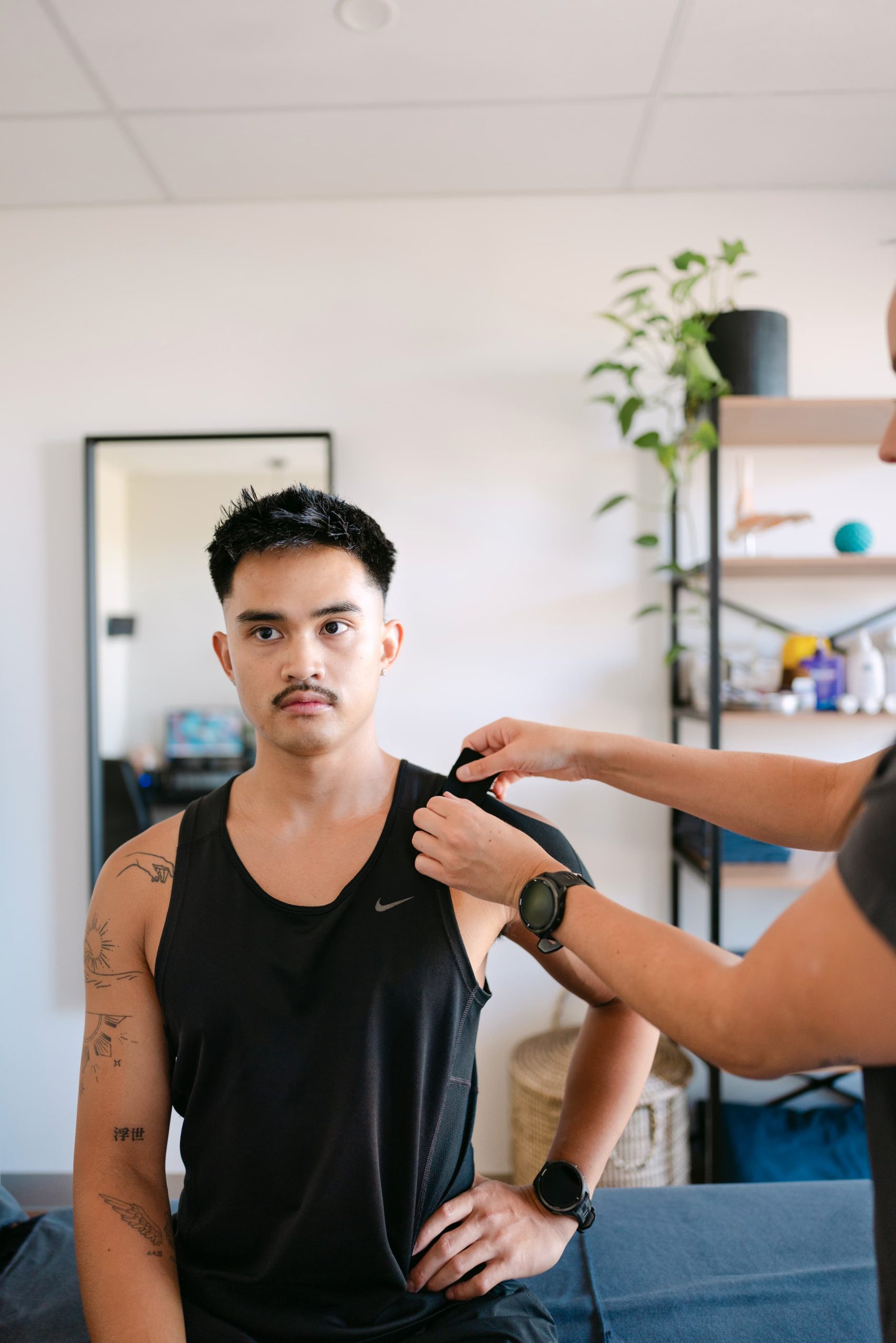 Live Well practitioner applying kinesio tape to patient's shoulder for muscle strain support