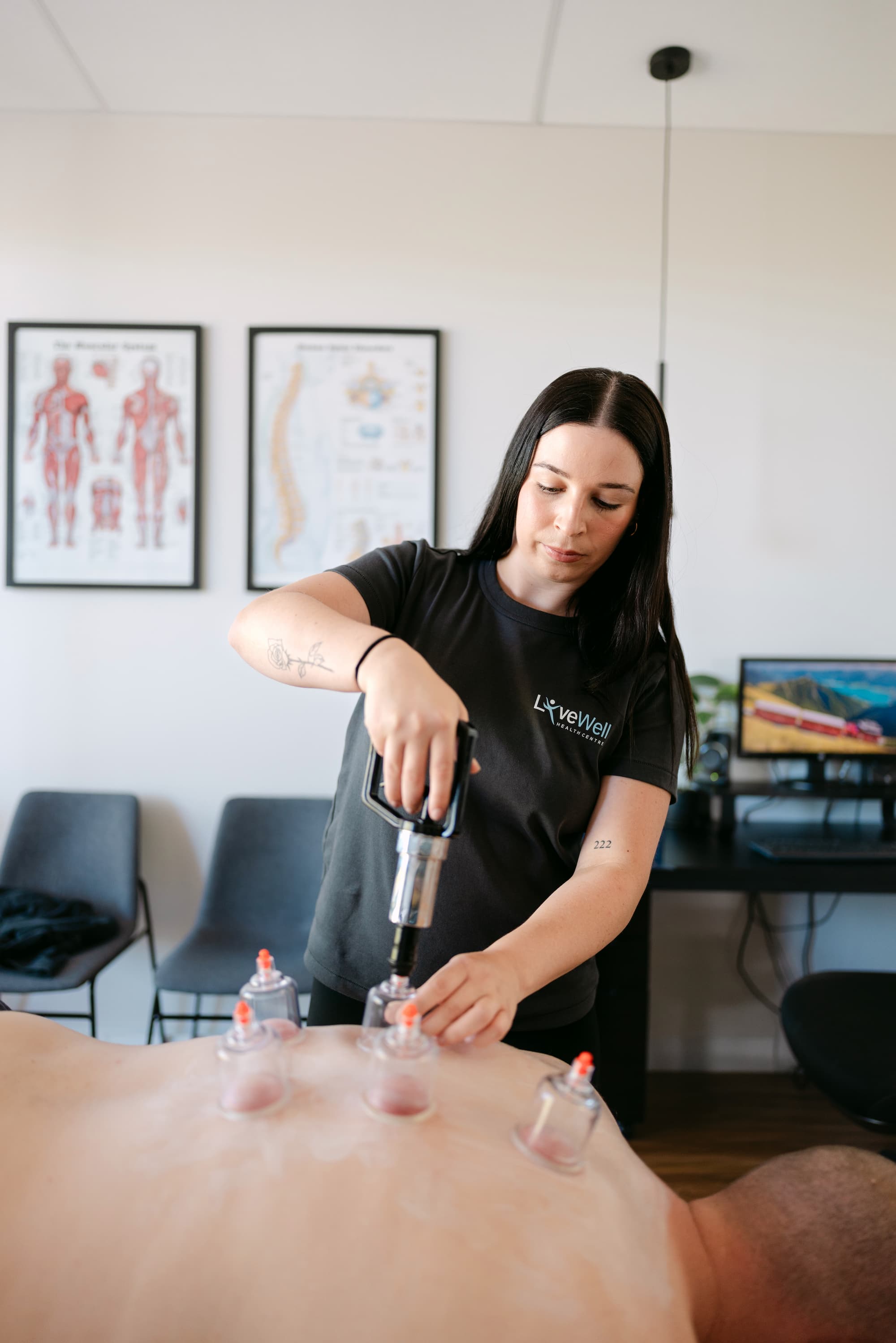 Live Well practitioner applying cupping therapy to patient's back using suction pump in clinic