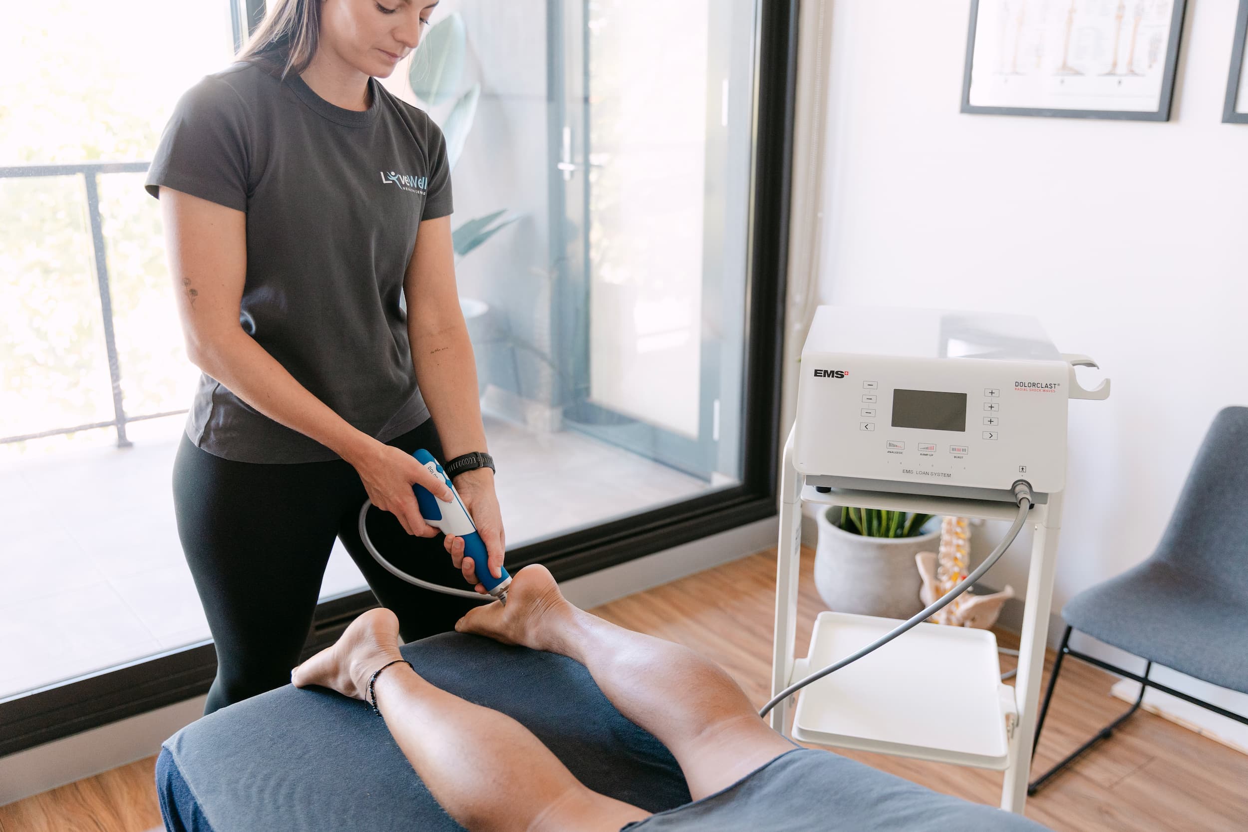 Live Well practitioner applying EMS shockwave therapy to patient's heel for plantar fasciitis relief