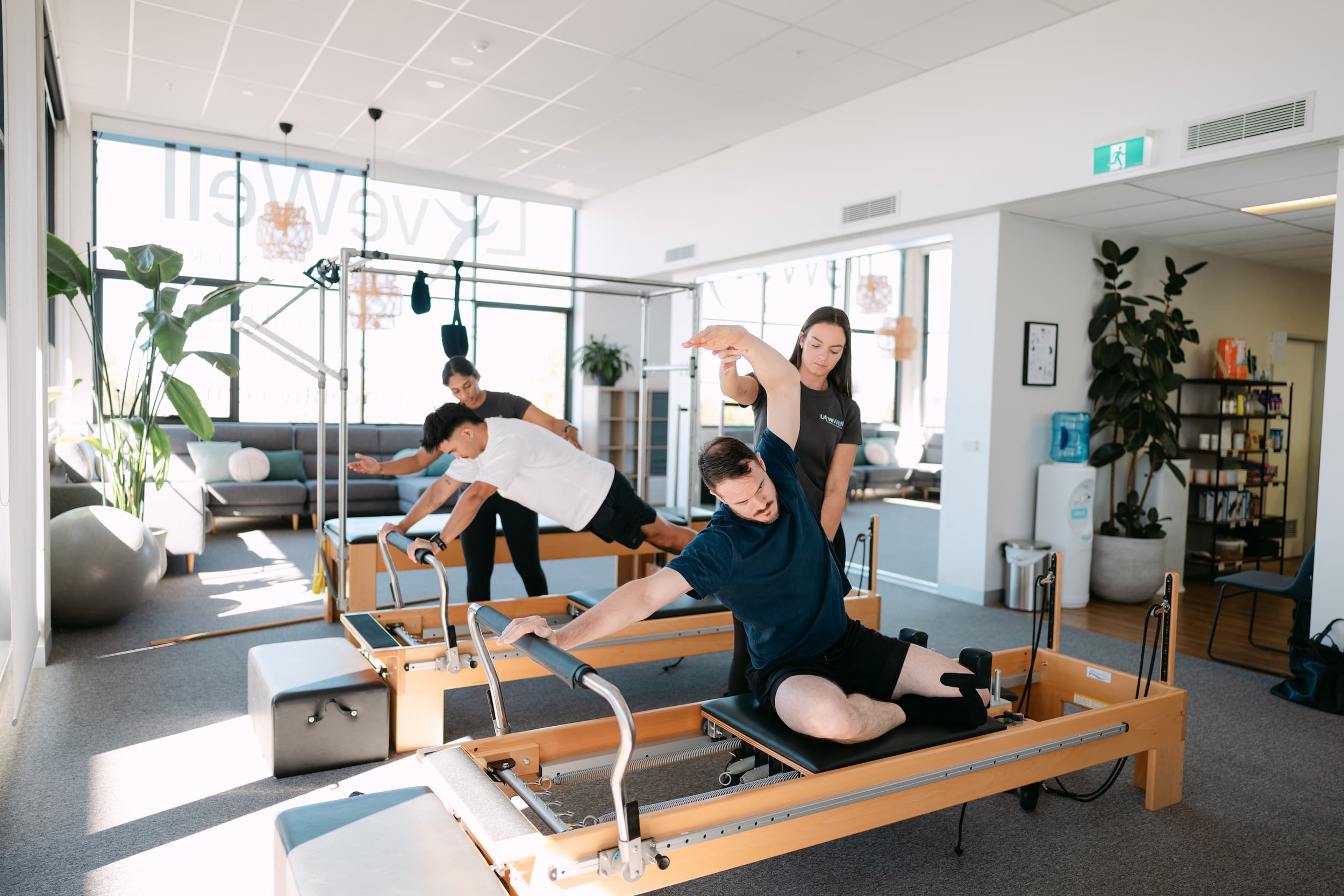 Live Well practitioners guiding two patients through spinal extension exercises on Pilates reformers