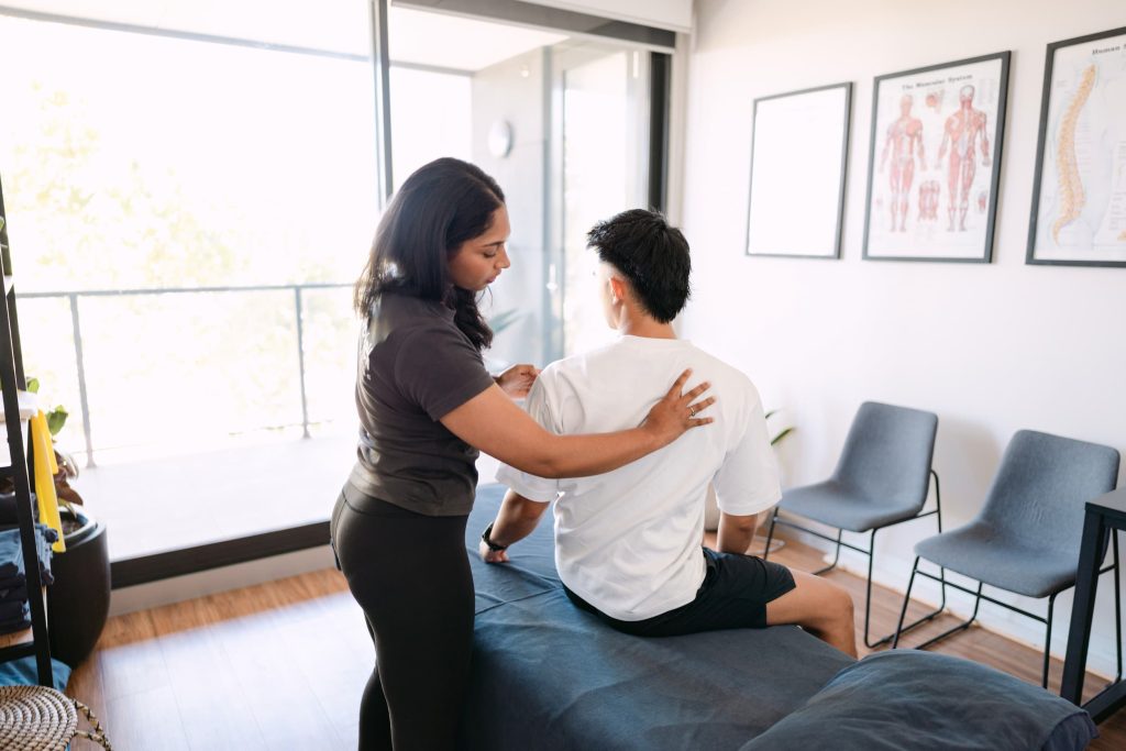 Live Well practitioner assessing patient's shoulder and upper spine on treatment table in clinic