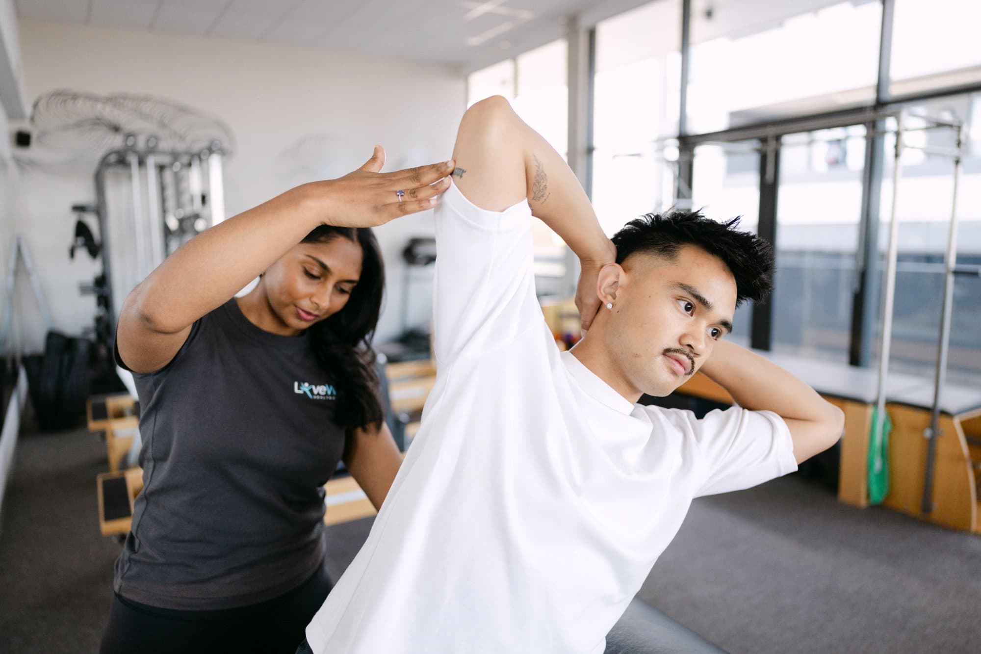 Live Well practitioner guiding patient through assisted lateral stretch in Pilates studio