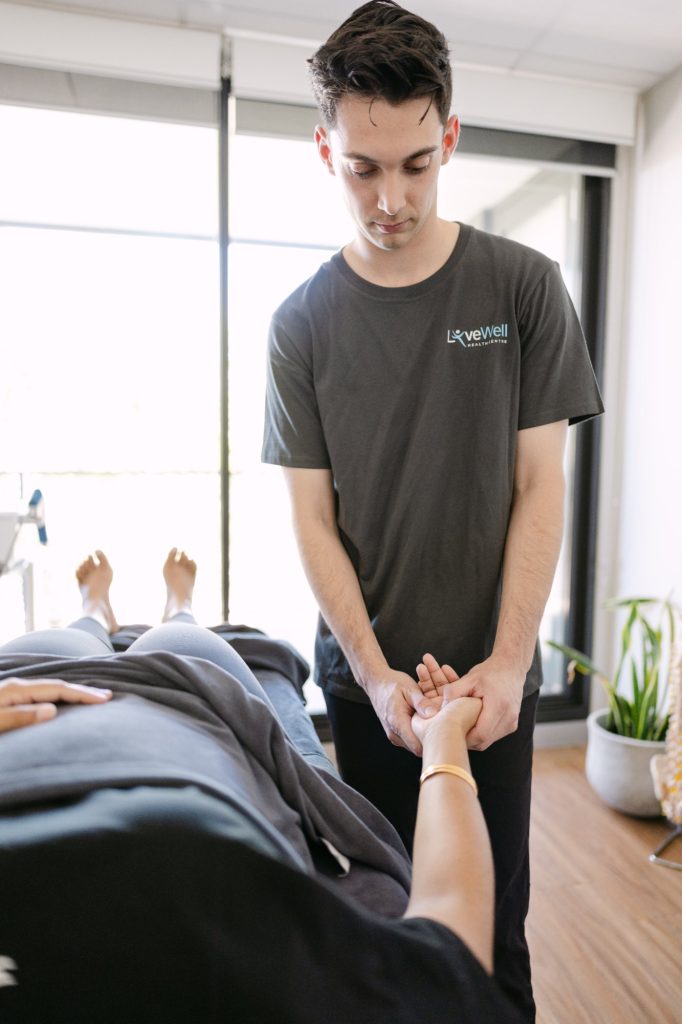 Live Well osteopath performing wrist mobilisation on patient lying on treatment table in clinic