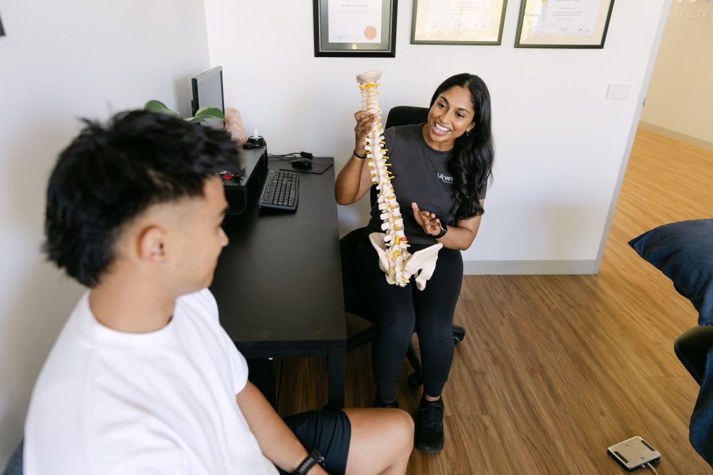 Osteopath explains spine model during posture assessment consultation at Live Well Health Centre.