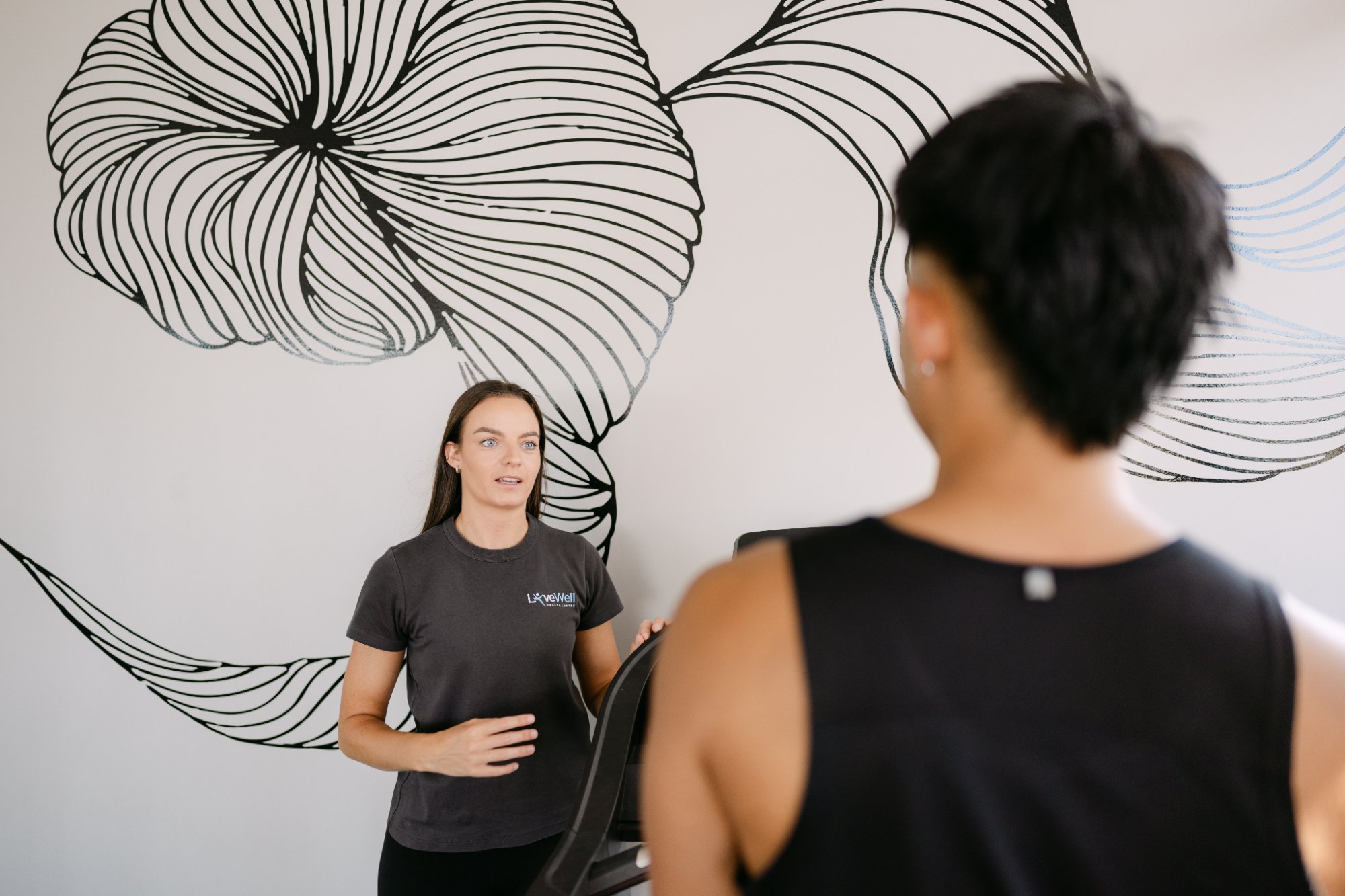 Live Well practitioner explaining frozen shoulder treatment plan to patient in modern gym studio