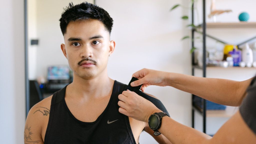 Live Well practitioner applying therapeutic tape to seated patient's shoulder for frozen shoulder treatment