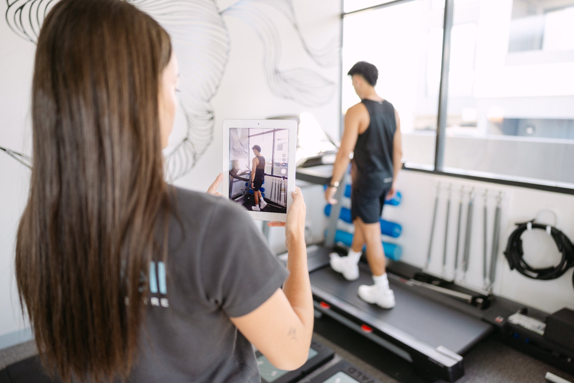 Live Well practitioner recording patient's treadmill gait analysis on tablet for ITB syndrome assessment