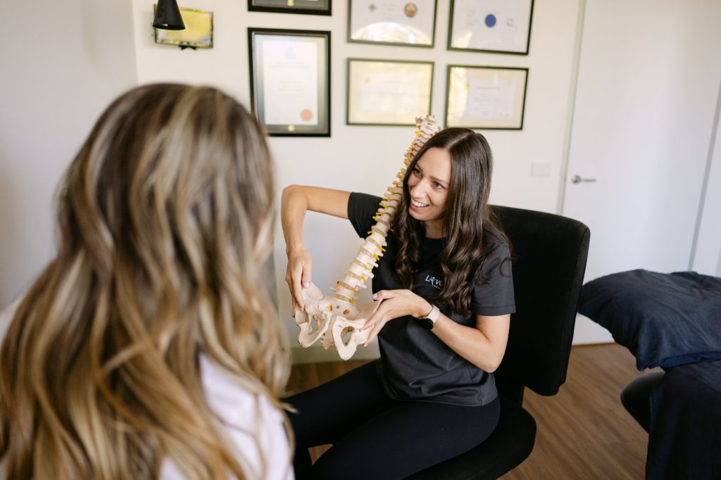 Smiling Live Well practitioner showing spinal and pelvis model to patient during pregnancy pelvic pain consultation