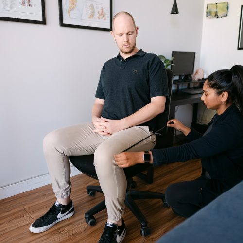 Live Well practitioner performing neurological reflex assessment on seated patient in clinic room