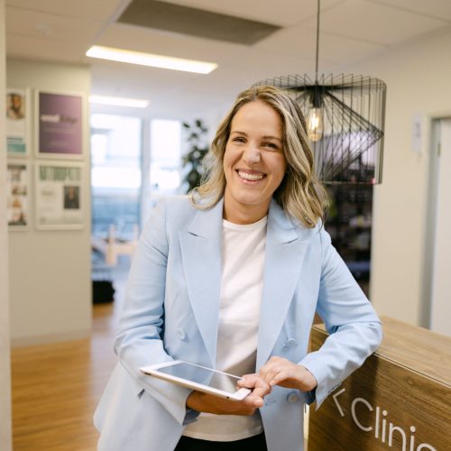 Karolina Kowalczyk – Director, Live Well Health Centre Karolina Kowalczyk, Director of Live Well Health Centre, smiling at clinic reception desk