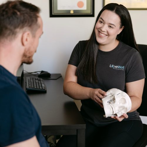 Live Well practitioner using skull model to explain TMJ dysfunction and jaw pain to patient